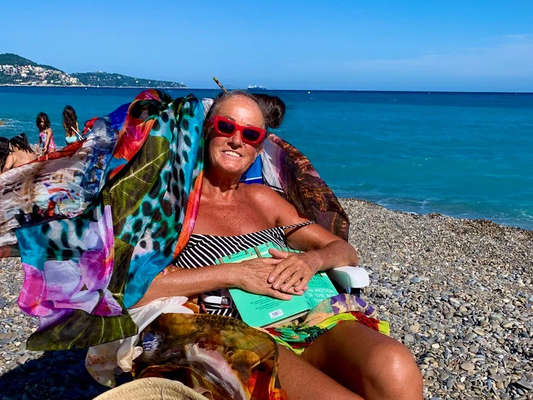 woman sitting on sun lounger that has colourful silk scarves tied to it.