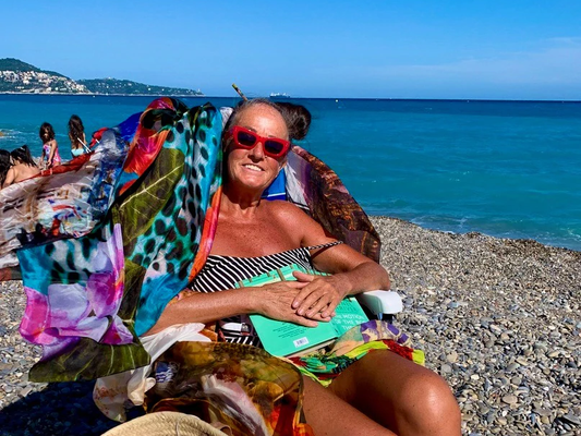 woman sitting on sun lounger that has colourful silk scarves tied to it. 